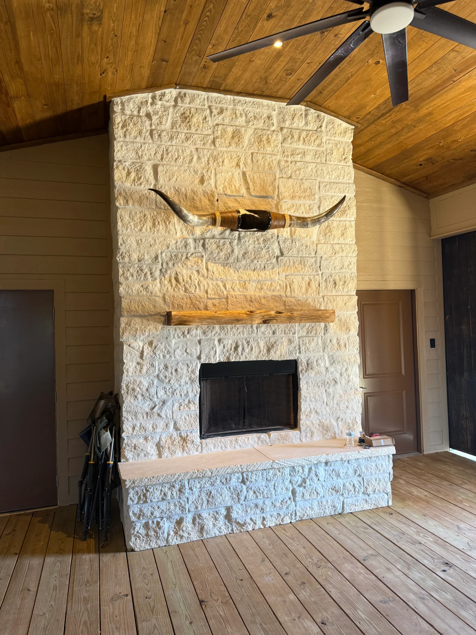 Cream rough-faced stacked stone fireplace with live-edge wood mantel, black metal fireplace door, and wood plank ceiling