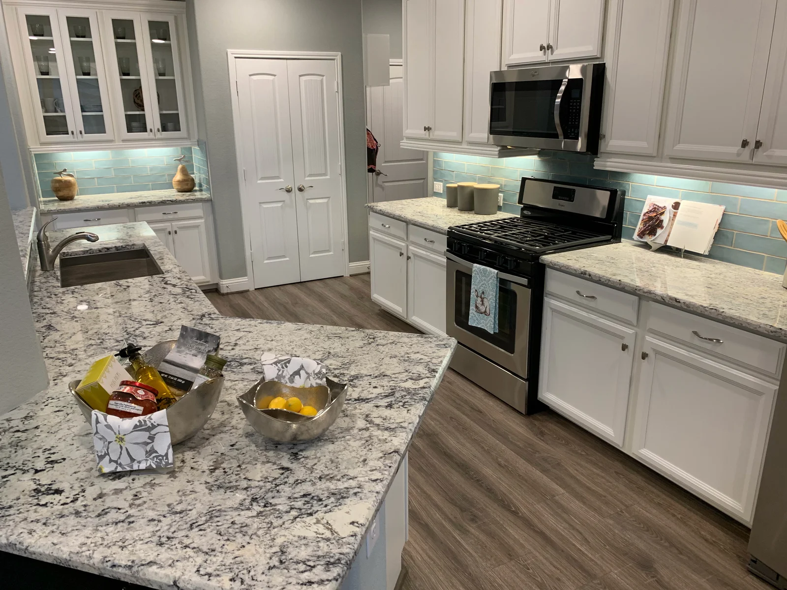 Kitchen with white cabinets, white veined granite countertops, aqua subway tile backsplash, and stainless steel gas range