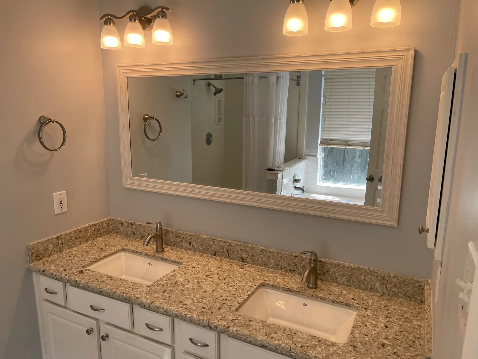 Double vanity with white cabinets, speckled countertop, undermount sinks, brushed nickel faucets, and framed mirror