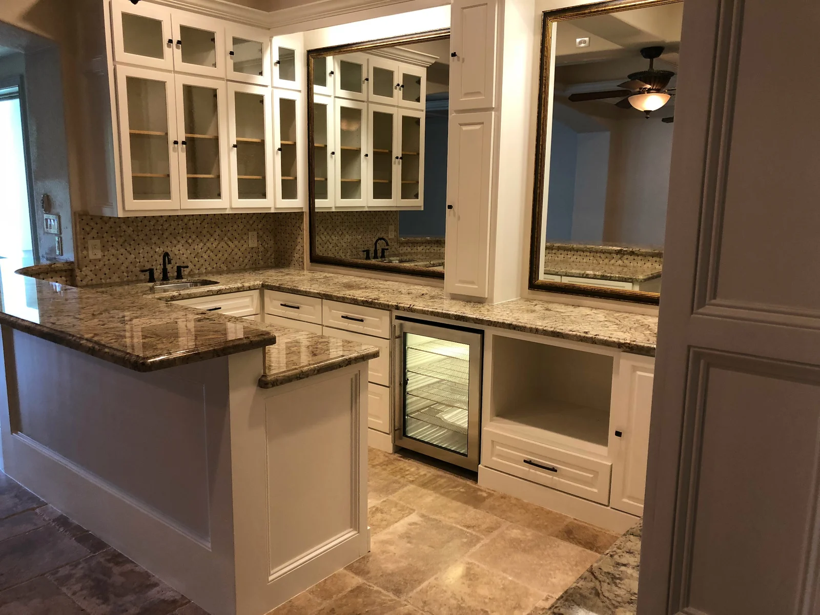 White glass-front cabinets, granite counters, mosaic stone backsplash, and built-in beverage fridge in a wet bar remodel