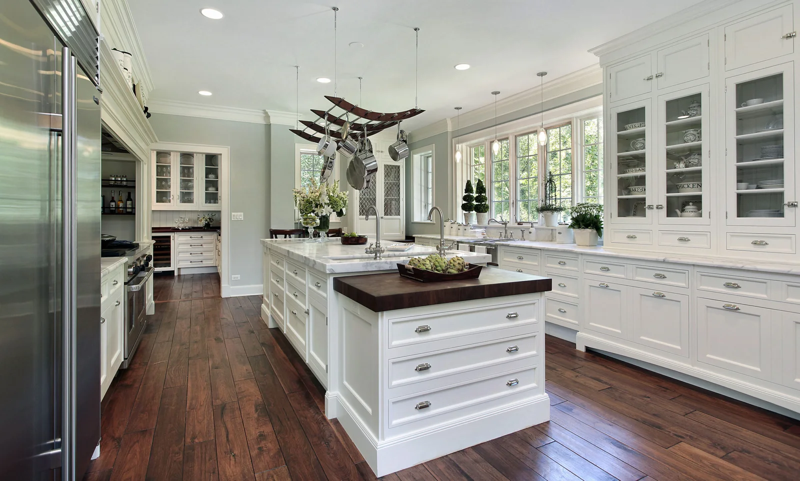 White painted kitchen with glass-front cabinets, dark wood island top, marble counters, and wide-plank hardwood floors